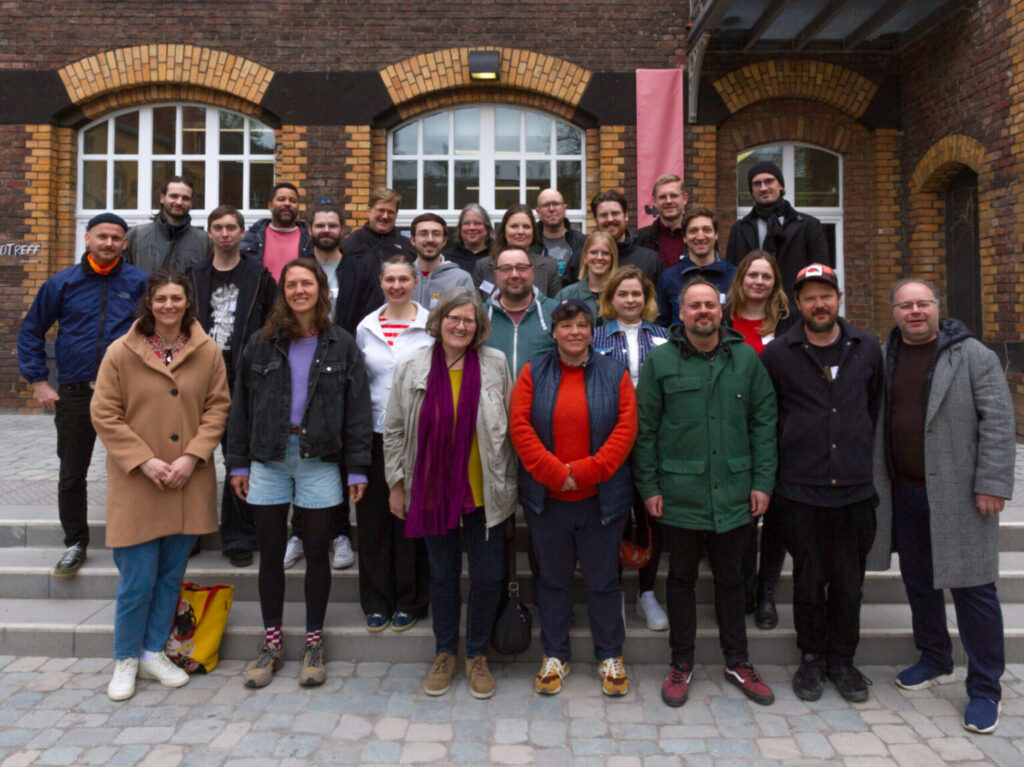 Ein Gruppenfoto von ca 30 Menschen, alle mit Jacken, auf einer Treppe vor einem Backsteingebäude.